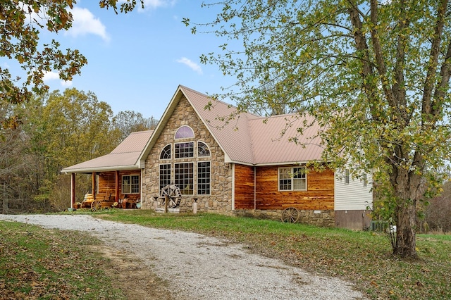 view of front facade with driveway, covered porch, stone siding, and metal roof