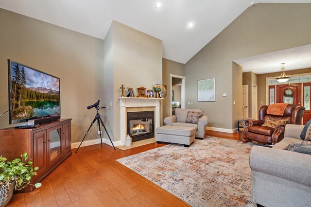 living room featuring high vaulted ceiling, light wood-style flooring, baseboards, and a fireplace with flush hearth