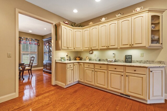 kitchen featuring light wood finished floors, glass insert cabinets, visible vents, and baseboards