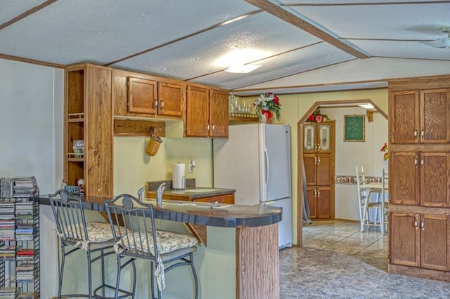 5088 Baptist Ridge Rd, Hilham, TN 38568 - kitchen with vaulted ceiling, brown cabinetry, a kitchen bar, freestanding refrigerator, and a peninsula
