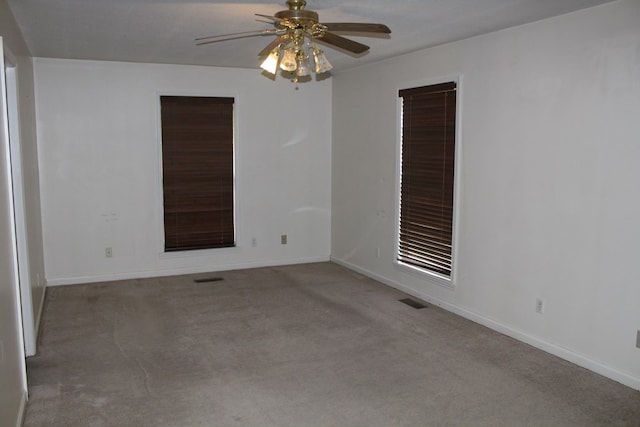 empty room with visible vents, baseboards, a ceiling fan, and light colored carpet