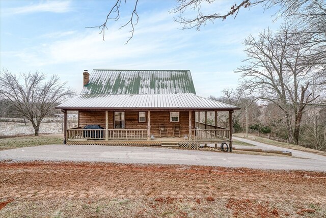 view of front of property with metal roof, a chimney, and a porch