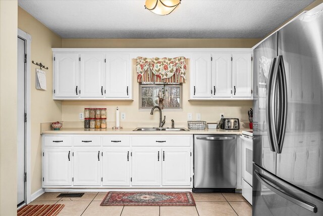 kitchen with light tile patterned floors, light countertops, appliances with stainless steel finishes, white cabinetry, and a sink