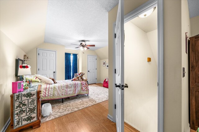 bedroom featuring lofted ceiling, ceiling fan, light wood-style flooring, and a textured ceiling