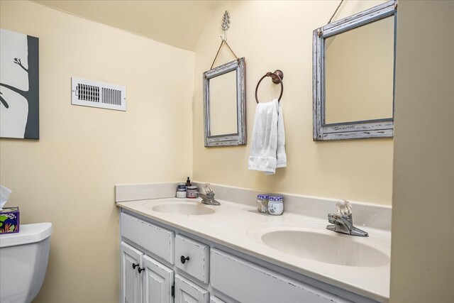 bathroom with toilet, double vanity, a sink, and visible vents