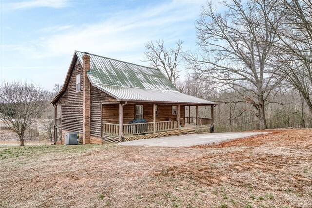 view of front of home with a porch, central AC, metal roof, and a chimney