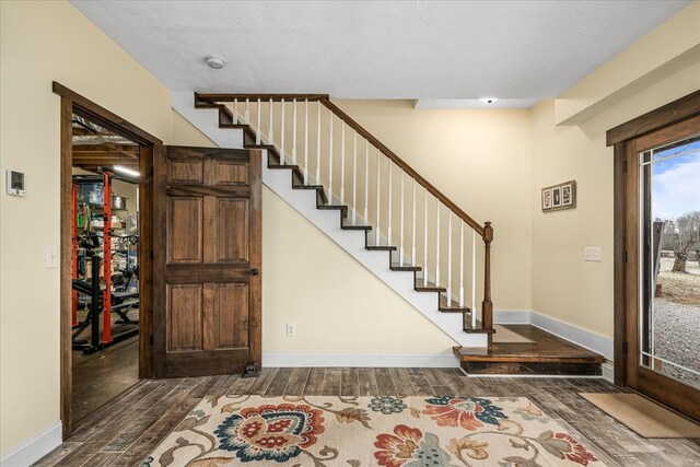 foyer entrance with stairs, dark wood-type flooring, a textured ceiling, and baseboards