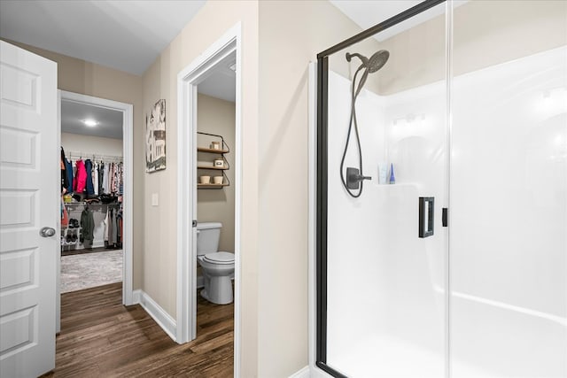 bathroom featuring a stall shower, baseboards, toilet, wood finished floors, and a walk in closet