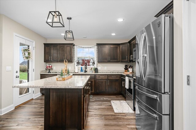 kitchen with light stone counters, dark brown cabinetry, stainless steel appliances, a center island, and pendant lighting