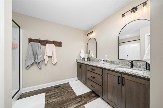 bathroom with double vanity, baseboards, wood finished floors, a shower stall, and a sink