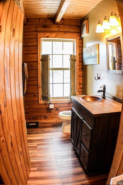 bathroom featuring toilet, wooden walls, wood finished floors, vanity, and wood ceiling