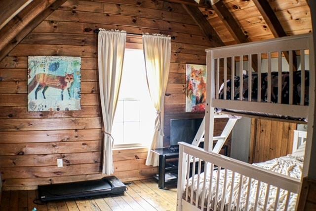 bedroom with vaulted ceiling with beams, wood walls, wooden ceiling, and wood finished floors