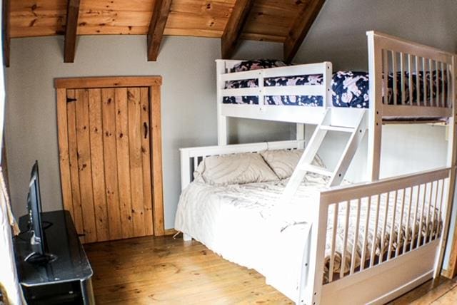 bedroom with vaulted ceiling with beams, wooden ceiling, and wood finished floors