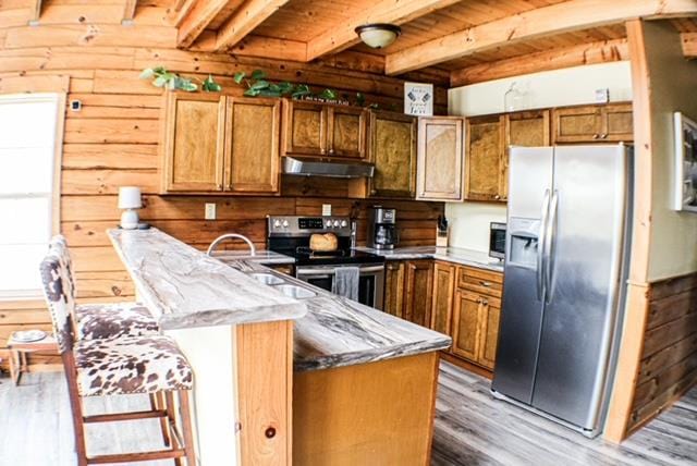 kitchen with beam ceiling, brown cabinets, stainless steel appliances, light wood-type flooring, and under cabinet range hood