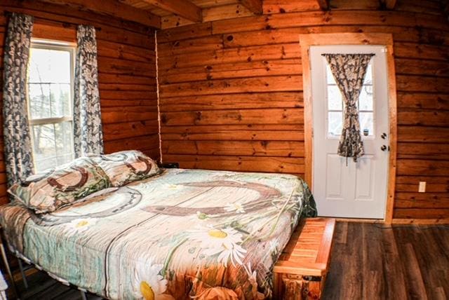 unfurnished bedroom with dark wood-type flooring, beam ceiling, and wood walls