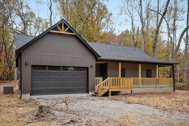 view of front facade with a porch, an attached garage, central air condition unit, a shingled roof, and dirt driveway