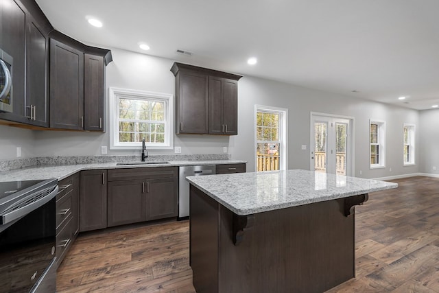 kitchen with dark wood-type flooring, stainless steel dishwasher, a kitchen bar, a sink, and range with electric stovetop