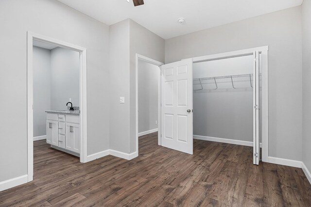 unfurnished bedroom featuring a sink, a closet, baseboards, and dark wood-style flooring