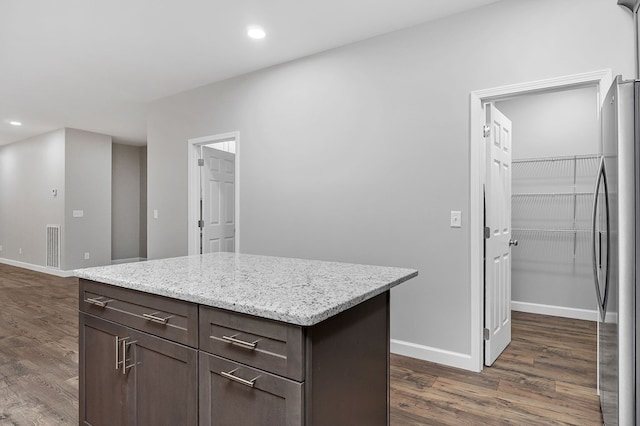 kitchen featuring dark wood-type flooring, freestanding refrigerator, a kitchen island, and baseboards