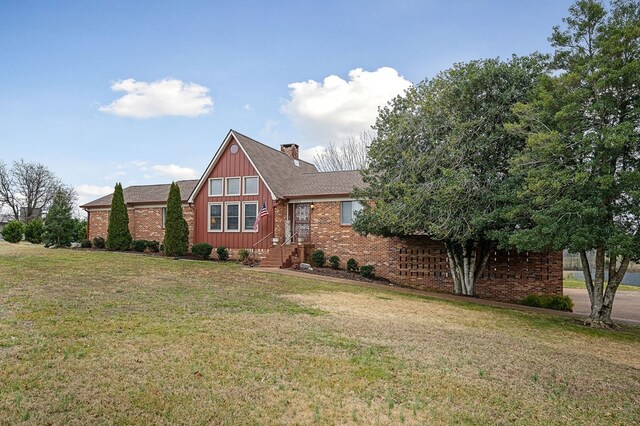 view of front of home with a front yard, a chimney, and brick siding