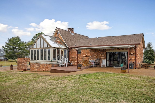 rear view of house featuring brick siding, a yard, a chimney, a patio, and a sunroom