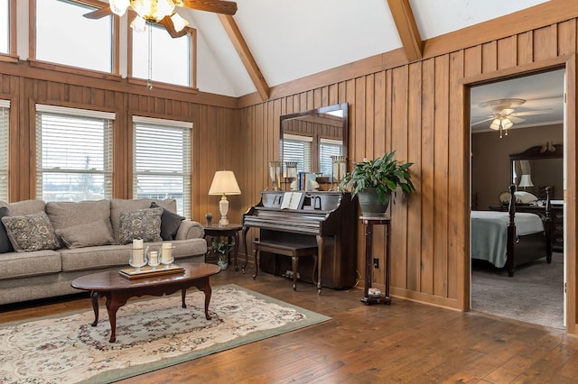 living room with dark wood-style floors, ceiling fan, beam ceiling, and wooden walls