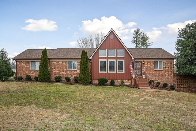 view of front of house featuring a shingled roof, a front lawn, board and batten siding, and brick siding