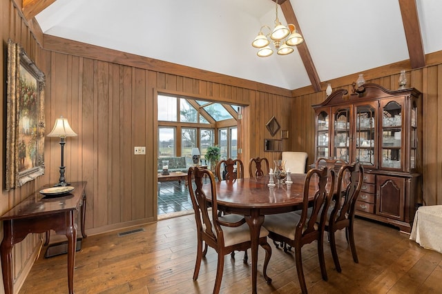 dining room with dark wood finished floors, a notable chandelier, visible vents, wooden walls, and high vaulted ceiling