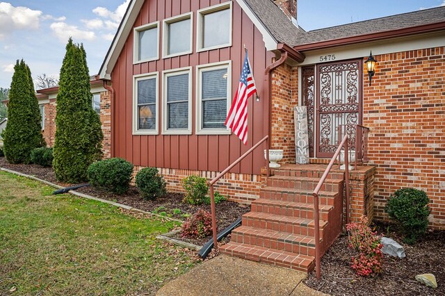 entrance to property with brick siding, board and batten siding, and a lawn