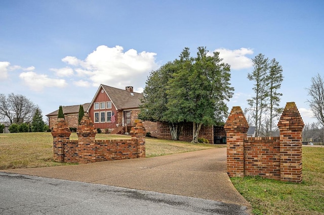 tudor home with a chimney, roof with shingles, a front yard, board and batten siding, and brick siding