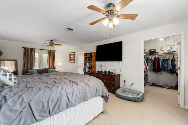 bedroom featuring a textured ceiling, light carpet, visible vents, a ceiling fan, and a walk in closet