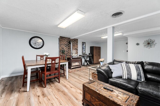 living room featuring a wood stove, light wood-style flooring, visible vents, and a textured ceiling