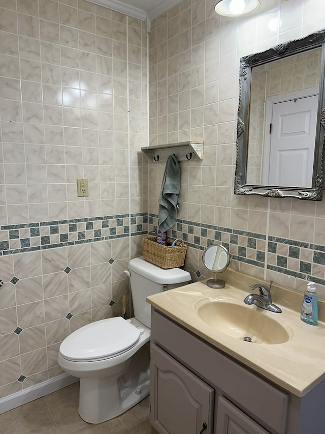 half bath featuring tile patterned flooring, crown molding, toilet, vanity, and tile walls