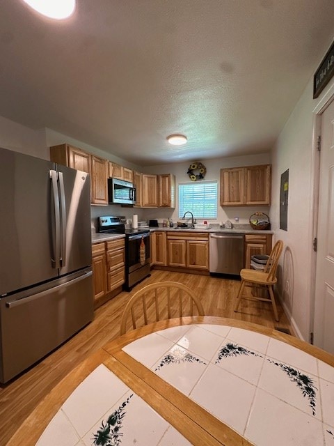 kitchen featuring light tile patterned floors, brown cabinetry, appliances with stainless steel finishes, a textured ceiling, and a sink