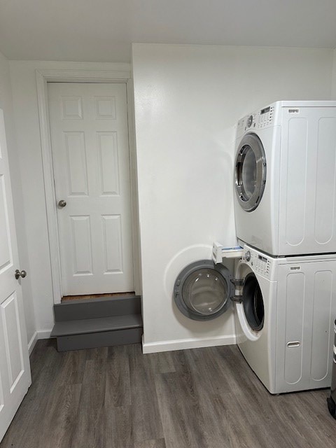 clothes washing area with stacked washer and dryer, baseboards, laundry area, and wood finished floors