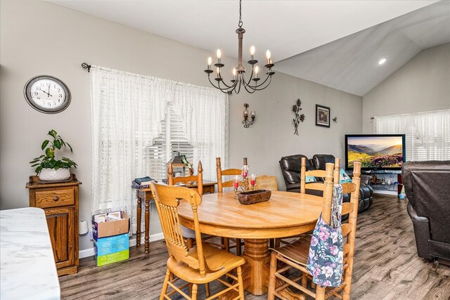 dining room featuring an inviting chandelier, vaulted ceiling, wood finished floors, plenty of natural light, and baseboards