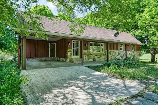 ranch-style house featuring board and batten siding, a shingled roof, concrete driveway, stone siding, and a carport