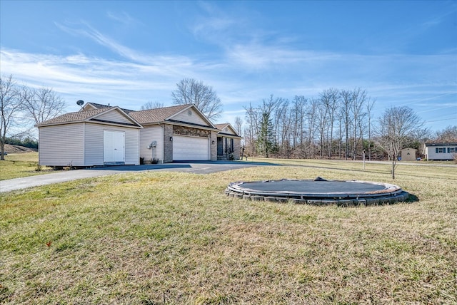 exterior space featuring driveway, an attached garage, a trampoline, and a yard