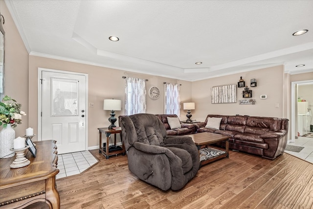 living area with a textured ceiling, a raised ceiling, wood finished floors, and crown molding