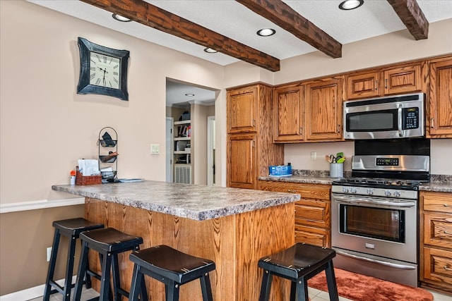 kitchen with baseboards, a kitchen breakfast bar, appliances with stainless steel finishes, brown cabinetry, and beamed ceiling