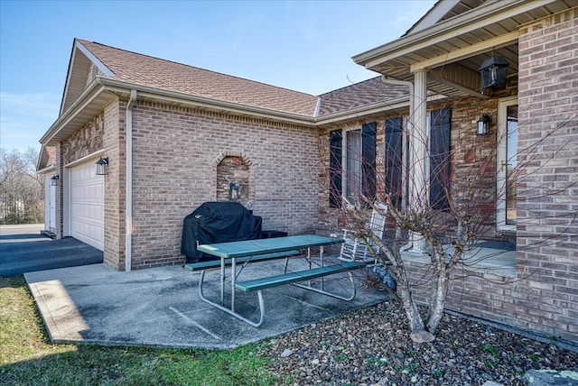 view of side of property with a garage, driveway, brick siding, and roof with shingles