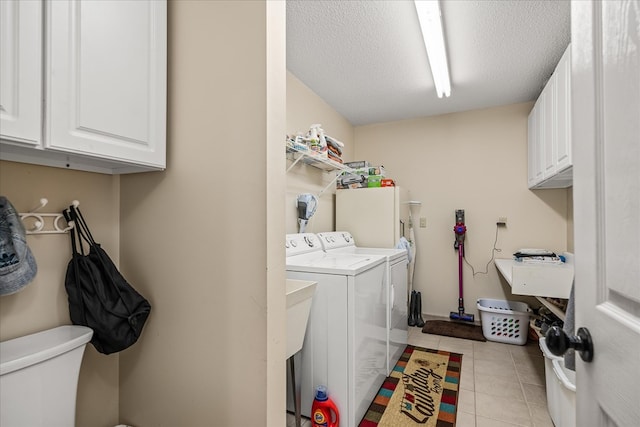 clothes washing area featuring a textured ceiling, light tile patterned flooring, a sink, cabinet space, and washing machine and clothes dryer