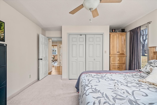 bedroom with light carpet, ceiling fan, a textured ceiling, and a closet