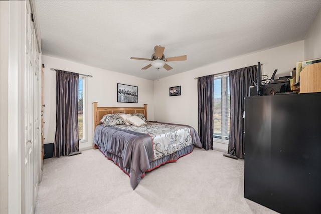 bedroom featuring a ceiling fan, light colored carpet, and a textured ceiling