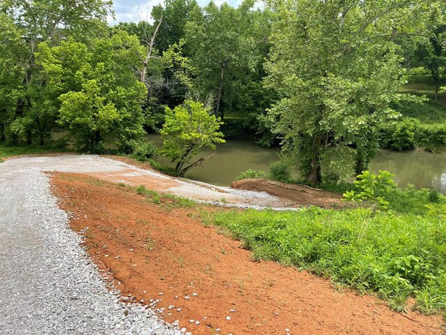 exterior space featuring a water view, a wooded view, and gravel driveway