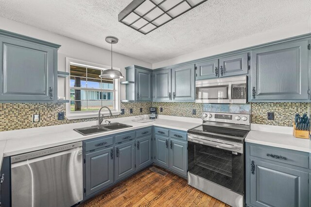 kitchen with stainless steel appliances, pendant lighting, light countertops, and a sink