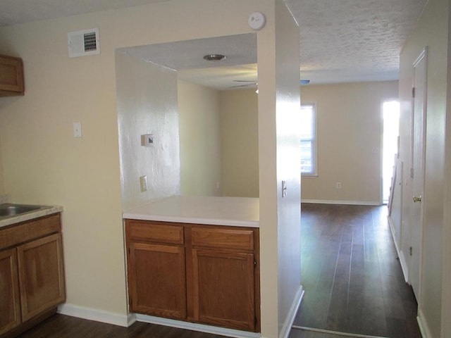 kitchen with dark wood finished floors, brown cabinets, a textured ceiling, light countertops, and baseboards