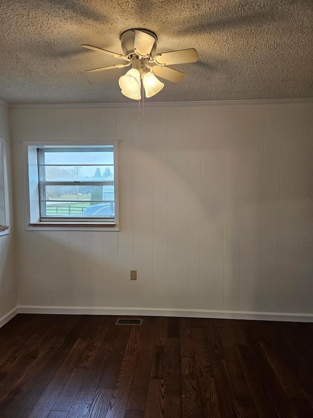 empty room with visible vents, a ceiling fan, dark wood-type flooring, crown molding, and a textured ceiling