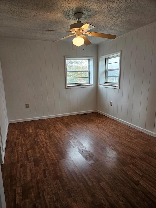 empty room featuring a textured ceiling, ceiling fan, dark wood-type flooring, and baseboards