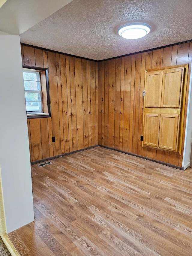 spare room with a textured ceiling, light wood-type flooring, visible vents, and wooden walls